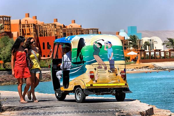 Zwei Frauen am Hotel Chedi El Gouna mit einem Golf-Auto, das am Wasser steht.