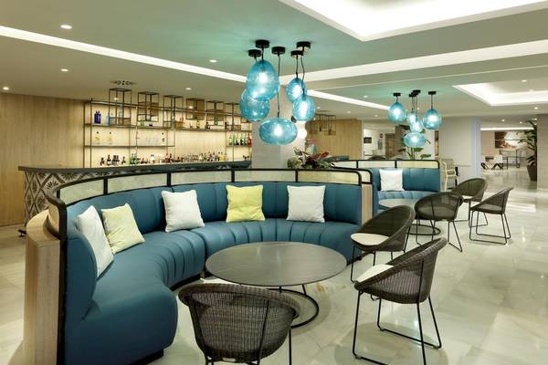 Loungebereich des Playabonita Hotels mit blauen Sofas, schwarzen Stühlen und runden Tischen.
