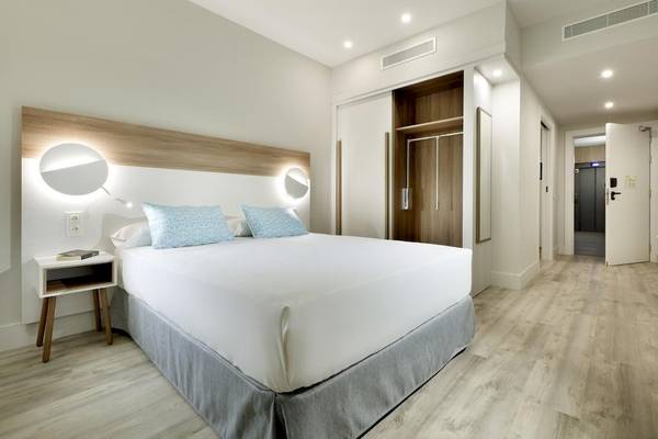 Schlafzimmer im Playabonita Hotel mit weißem Bett, Holzboden und Nachttisch