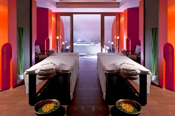 Behandlungsraum im Dusit Thani Krabi Beach Resort Spa mit zwei Massagetischen, roten Wänden und weißen Handtüchern.