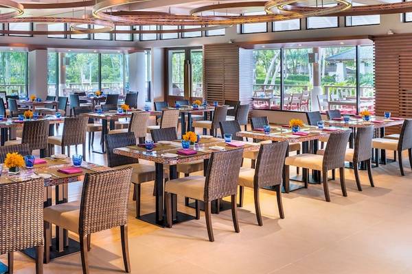 Innenansicht des Restaurants im Dusit Thani Krabi Beach Resort mit vielen gedeckten Tischen und Fenstern, die auf den Ozean blicken.