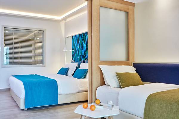 Innenansicht eines Hotelzimmers im Atlantica Aegean Blue Resort mit zwei Betten, Tisch und Früchten.