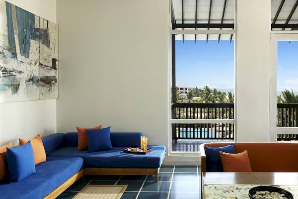 Wohnzimmer im Jetwing Blue Hotel mit blauem Sofa, Fenstern und Aussicht auf den Pool.