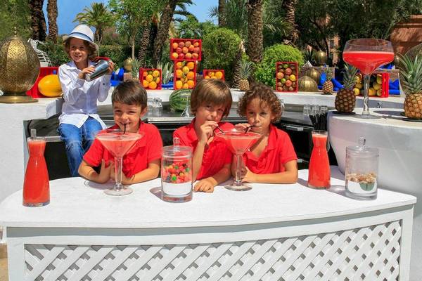 Kinder hinter einem Bartresen im Sofitel Marrakech Lounge & Spa mit selbstgemachten Getränken und Früchten im Hintergrund.