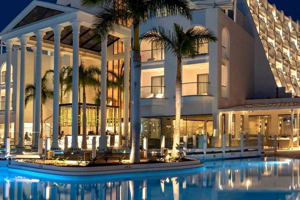 Die Guayarmina Princess Hotel Fassade ist beleuchtet und zeigt eine elegante Architektur mit Palmen und einem Pool vor dem Gebäude.