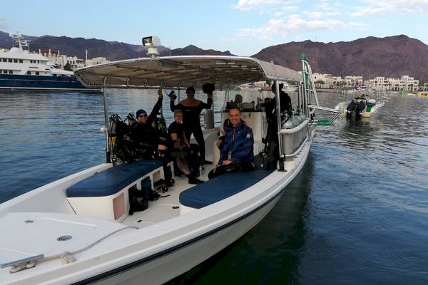 Taucher auf Boot vor Bergpanorama mit weiteren Booten im Hintergrund