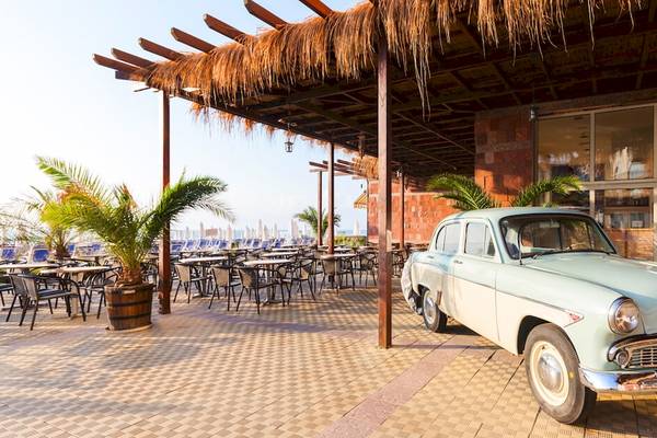 Altes Auto vor dem Sol Luna Bay Hotel mit Terrasse und Tischen.