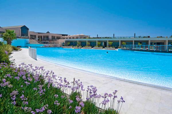 Außenpool des Giannoulis Cavo Spada Sports & Leisure Resort mit Gebäuden und Pflanzen im Hintergrund.