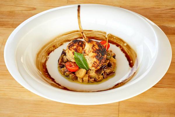 Ein Gericht in einem weißen Teller auf einem Holztisch mit gebratenem Fleisch, Gemüse und Sauce.