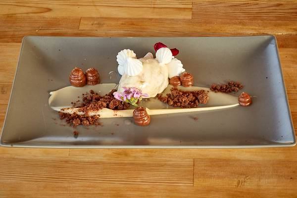 Ein Schokoladen-Dessert auf einem grauen Teller mit Eis, Schokoladenstücken und Blumendekor.