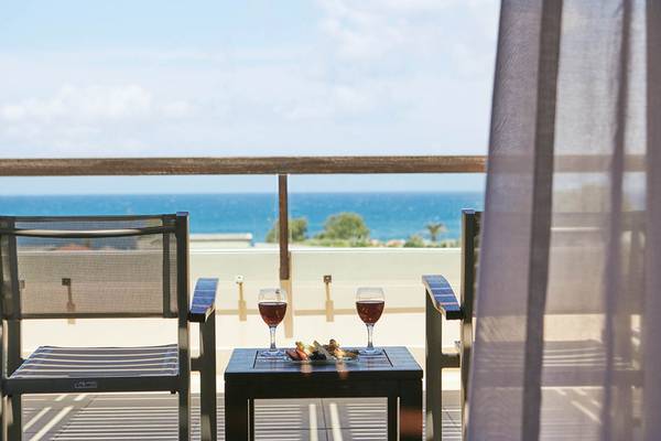 Auf dem Balkon des Giannoulis Cavo Spada Sports & Leisure Resorts mit Aussicht auf das Meer, zwei Gläsern Wein und Snacks.