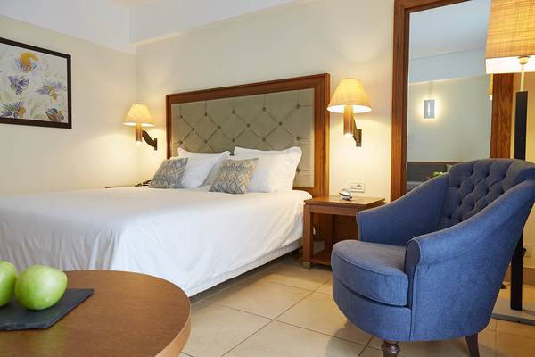 Ein Schlafzimmer im Giannoulis Cavo Spada Sports & Leisure Resort mit einem Bett, Kissen, Nachttischen, Lampen und einem Stuhl.