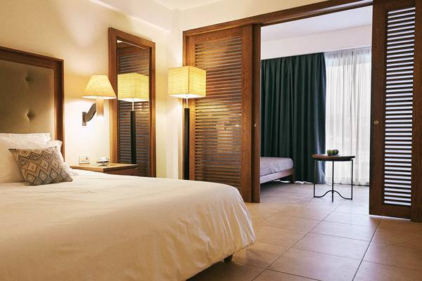 Schlafzimmer im Giannoulis Cavo Spada Sports & Leisure Resort mit Bett, Nachttischen und Wandlampen.