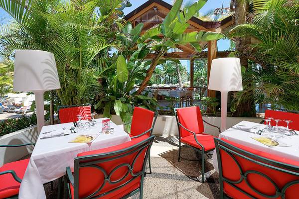 Außenbereich des Bull Costa Canaria & Spa Hotels mit roten Stühlen und Tischen, umgeben von Pflanzen.