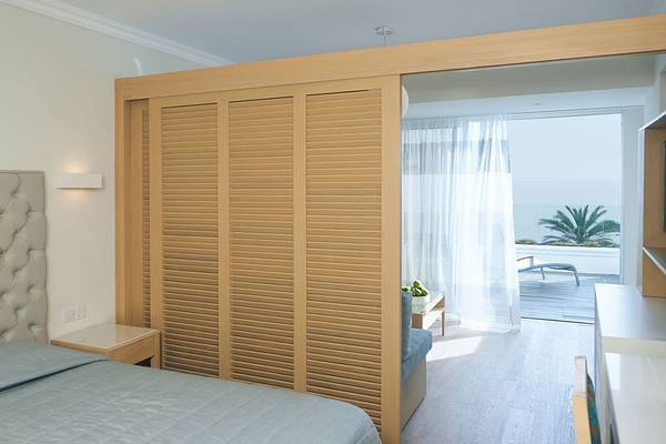 Schlafzimmer mit Aussicht auf das Meer im Sunrise Beach Hotel in Zypern, mit Holzschubladen, Bett und offenem Fenster.