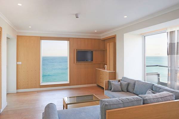 Wohnzimmer mit Meerblick im Sunrise Beach Hotel in Zypern, mit großer Couch, Glastisch und Fernseher.