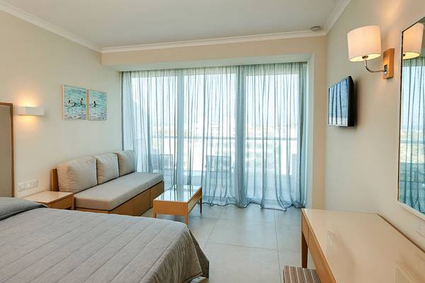 Hotelzimmer im Sunrise Beach Hotel in Zypern mit Doppelbett, Sofa, Tisch und großem Fenster.