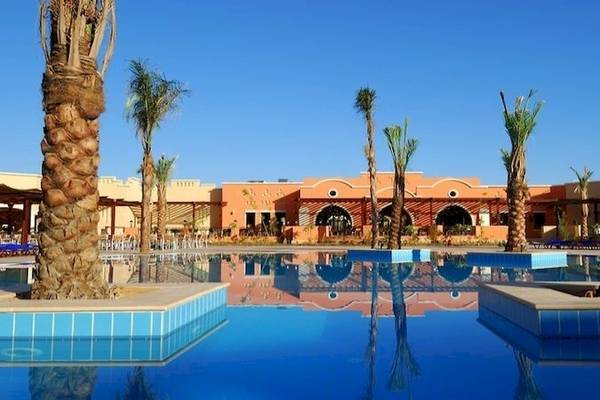Außenpool des JAZ Neo Dar El Madina Hotels mit Palmen und orangefarbenem Gebäude.