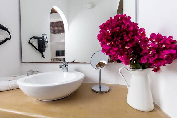 Badezimmer mit weißem Waschbecken, Spiegel und Blumenvase auf dem Waschtisch.