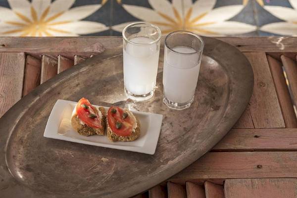 Ein Tisch mit zwei Gläsern weißer Flüssigkeit und einem kleinen Teller mit Tomatenscheiben im Rhenia Mykonos Hotel.