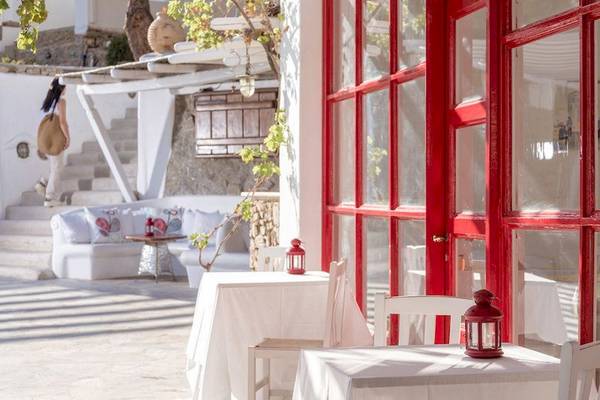 Terrasse des Rhenia Mykonos Hotel mit roten Fenstern und Tischen im Freien.