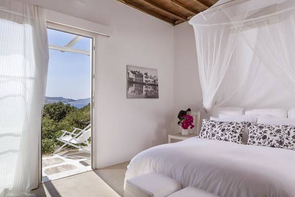 Schlafzimmer im Rhenia Mykonos Hotel mit Meerblick, weißen Wänden, offenen Türen und Balkon.