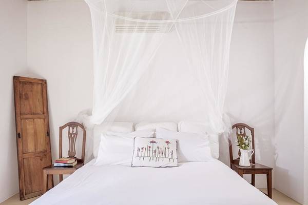 Schlafzimmer im Rhenia Mykonos Hotel mit weißem Bett, Kopfteil mit Netz, zwei Nachttischen und Holzmöbeln.