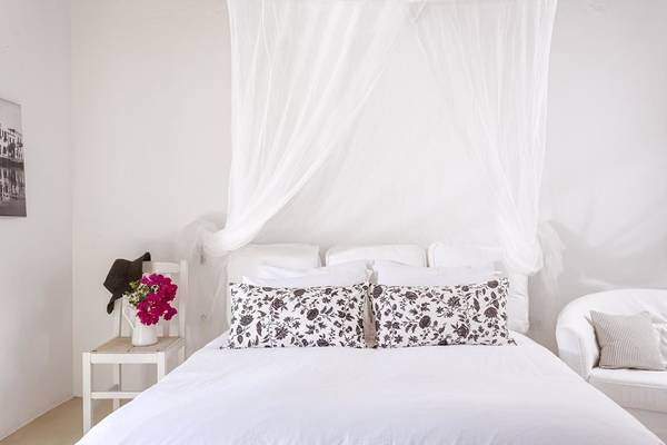 Weißes Schlafzimmer mit Bett, Blumenvase und Stuhl im Rhenia Mykonos Hotel.