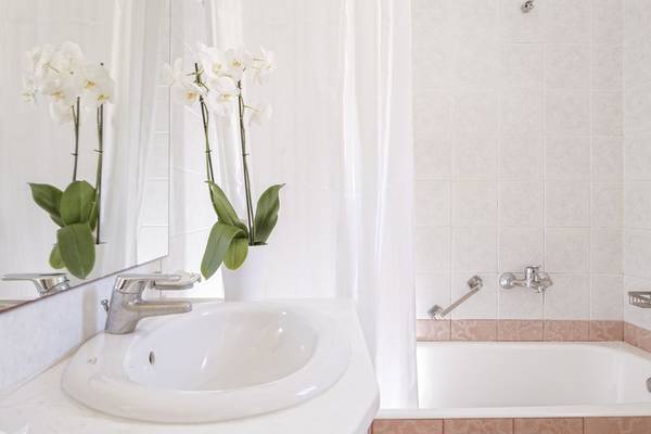Badezimmer des Rhenia Mykonos Hotel mit weißer Wanne, Spiegel und Orchideen.