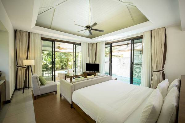 Innenansicht eines Schlafzimmers im Robinson Khao Lak Hotel mit Bett, Sofa, Fernseher und Swimmingpool im Hintergrund.