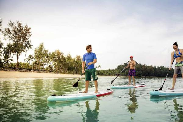 Drei Personen auf Stand-Up-Paddle-Brettern am Strand des Robinson Khao Lak Hotels.