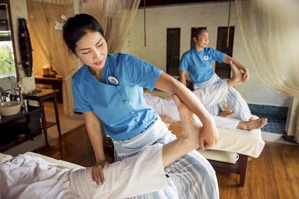 Massage im Robinson Khao Lak Hotel: Eine Frau massiert einen Mann, während eine andere im Hintergrund assistiert.