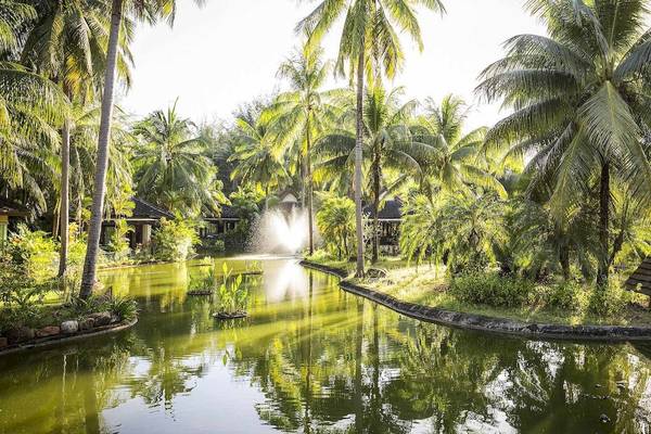Außenbereich des Robinson Khao Lak Resorts mit einem Teich und Palmen.
