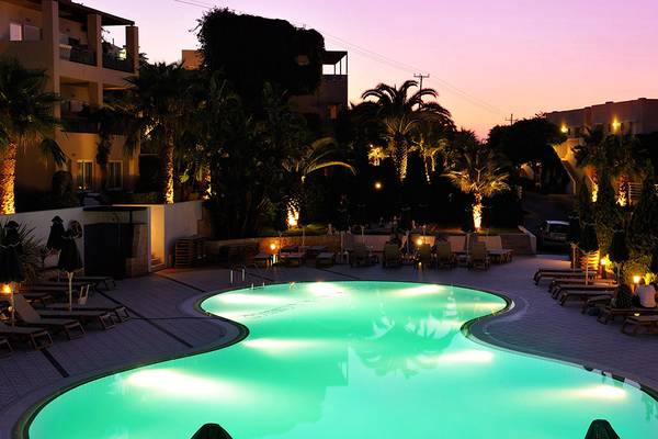 Ein Swimmingpool des Grand Hotel Holiday Resort bei Nacht, mit leuchtendem Wasser und umgeben von Liegestühlen und Palmen.
