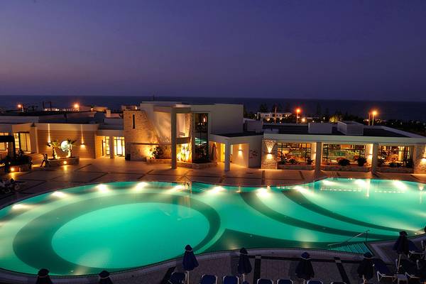 Grand Hotel Holiday Resort bei Nacht mit beleuchtetem Pool und Meer im Hintergrund.