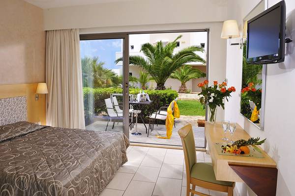 Innenansicht eines Zimmers im Grand Hotel Holiday Resort mit Bett, Schreibtisch und Balkon.
