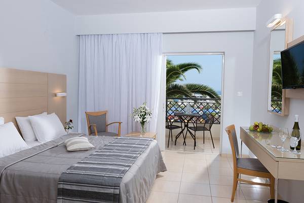 Innenansicht eines Hotelzimmers im Grand Hotel Holiday Resort mit Balkon, Bett, Tisch, Stühlen und Fernseher.