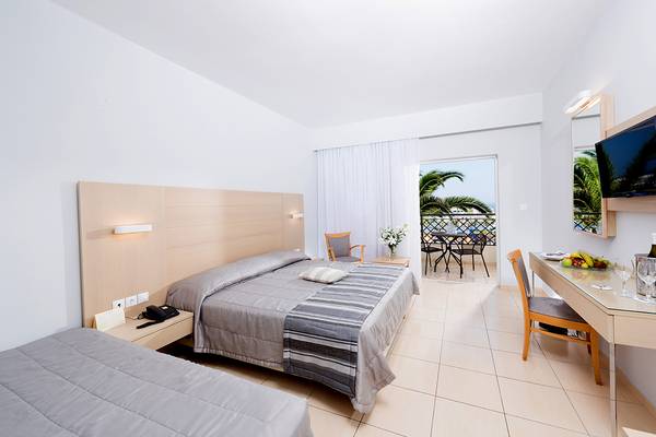 Innenansicht eines Zimmers im Grand Hotel Holiday Resort mit zwei Betten, einem Schreibtisch, einem Balkon und einem Fernseher.
