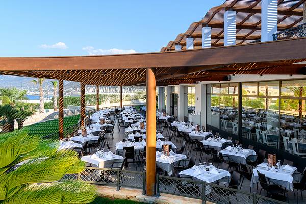 Restaurantterrasse des Grand Hotel Holiday Resort mit vielen Tischen und Stühlen, umgeben von Pflanzen und Aussicht auf das Meer.