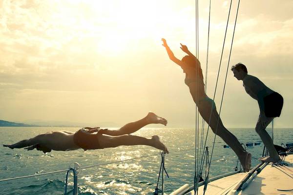 Zwei Frauen und ein Mann springen vom Segelboot ins Wasser.