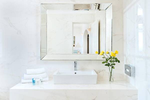 Badezimmer von Agali Houses mit weißem Waschbecken, Spiegel und gelben Rosen in einer Vase.