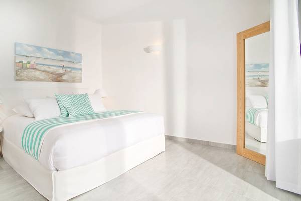 Innenansicht eines Hotelzimmers von Agali Houses mit weißem Bett, grünen Kissen und einer Wandmalerei.