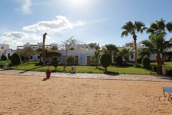 Außenansicht des Sharm Club Beach Resorts mit weißen Gebäuden und üppigem Garten