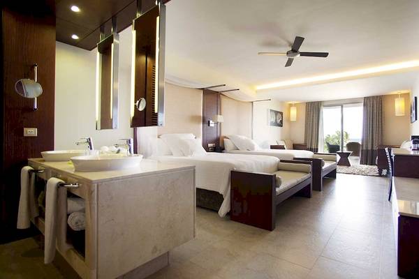 Innenansicht der Suite im Barcelo Bavaro Palace Hotel mit Doppelbetten, Badezimmer und Wohnzimmerbereich.