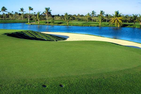 Golfplatz des Barcelo Bavaro Palace Hotel mit Wasserhindernis und Palmen im Hintergrund.