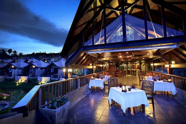 Außenbereich des Nora Buri Resorts & Spa bei Nacht mit gedeckten Tischen und leuchtenden Lampen.