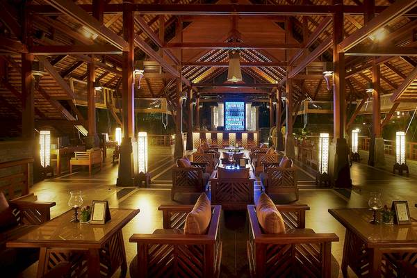 Innenbereich des Nora Buri Resorts & Spa mit Lounge-Bereich und beleuchteten Holzsäulen.