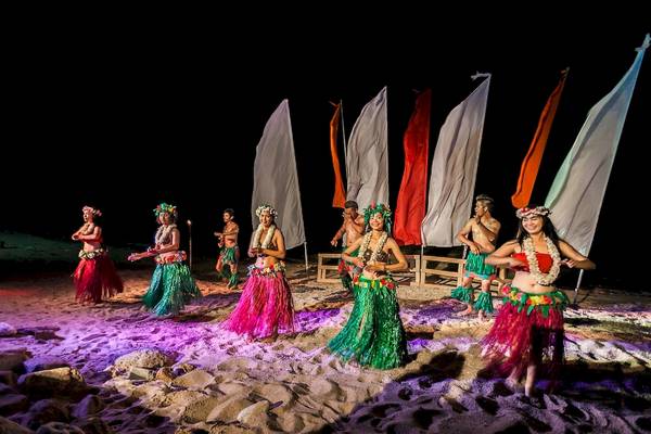 Gruppe von Hula-Tänzerinnen vor bunten Flaggen auf dem Strand