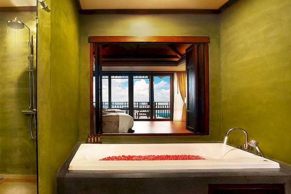 Badezimmer im Nora Buri Resort & Spa mit Badewanne, Regendusche und Fenster zum Balkon.