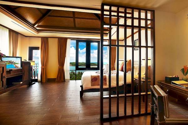 Innenansicht eines Hotelzimmers im Nora Buri Resort & Spa mit Bett, Schreibtisch und Aussicht auf den Ozean.